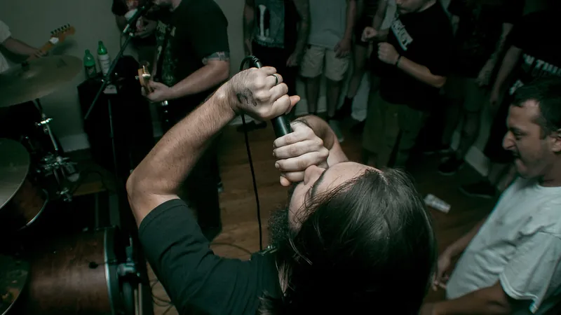 Cantante de una banda punk gritando al micrófono rodeado de público en un concierto pequeño