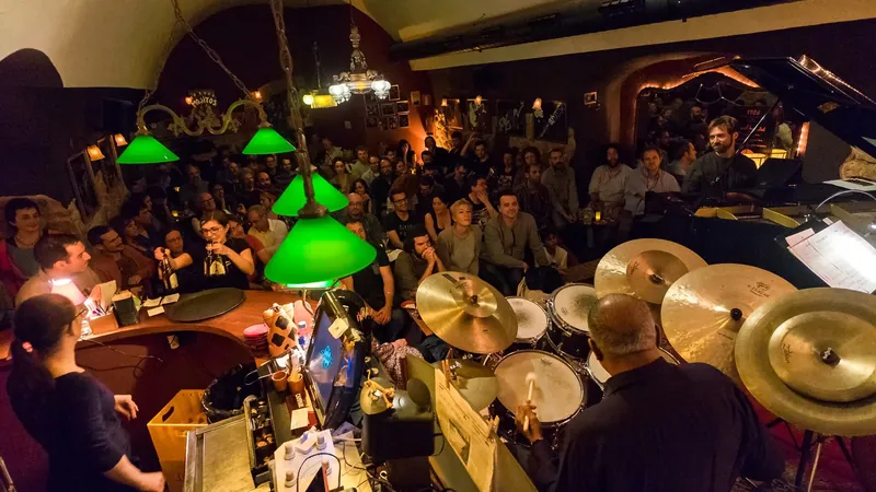 Club de jazz abarrotado visto desde el escenario, con batería en primer plano y lámparas verdes