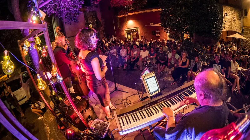 Cantante y pianista de jazz actuando al aire libre ante un público sentado bajo guirnaldas de bombillas en una noche de verano