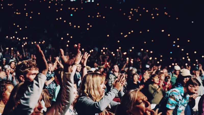 Público de un gran concierto con los brazos en alto y luces de móviles en la oscuridad