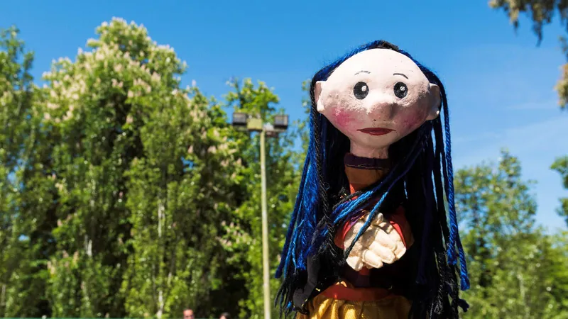 Marioneta de pelo azul y vestido amarillo en una función de títeres al aire libre entre árboles