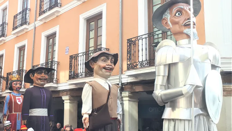 Comparsa de gigantes y cabezudos recorriendo una calle porticada entre vecinos