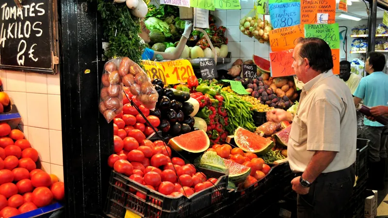 Puesto de frutas y verduras de colores en un mercado de abastos con un cliente mirando el género