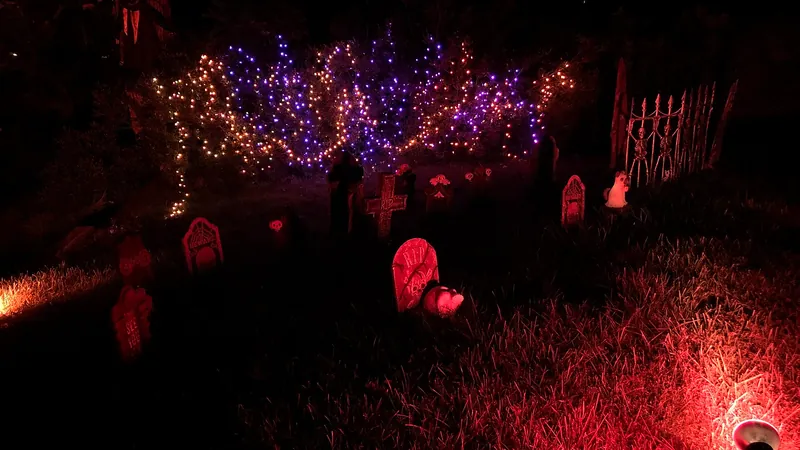 Jardín decorado para Halloween con lápidas iluminadas de rojo y guirnaldas de luces moradas y naranjas