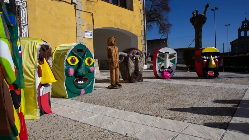 Máscaras y trajes de botarga expuestos en la plaza de un pueblo de la Alcarria, con la iglesia al fondo