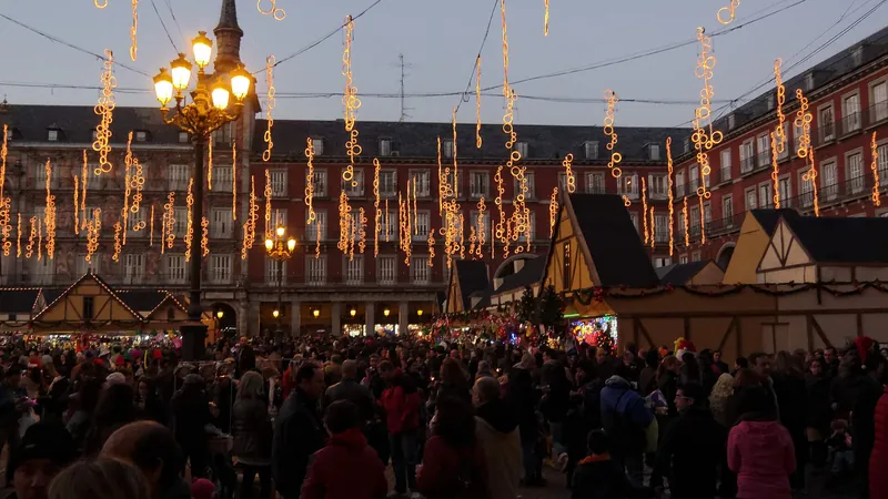 Mercado navideño de la Plaza Mayor de Madrid al anochecer, con casetas, guirnaldas de luces y mucha gente paseando