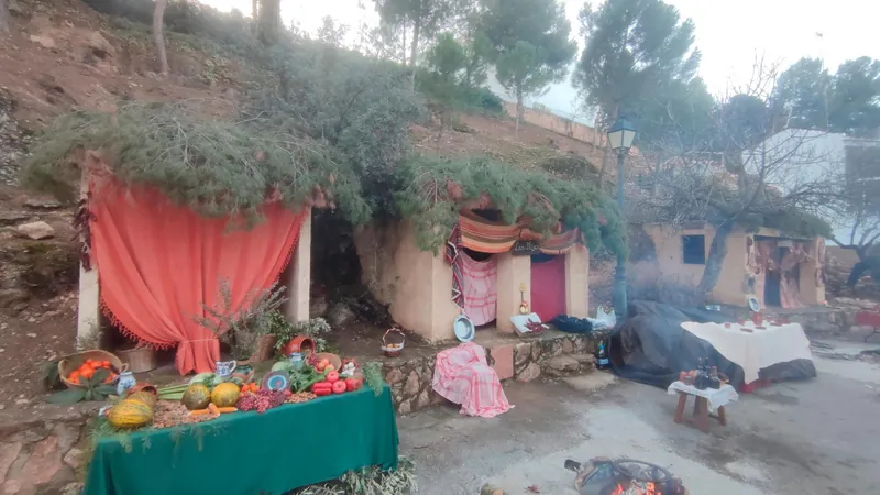Escenario de un belén viviente al aire libre con telas rojas, cestas de fruta y una pequeña hoguera