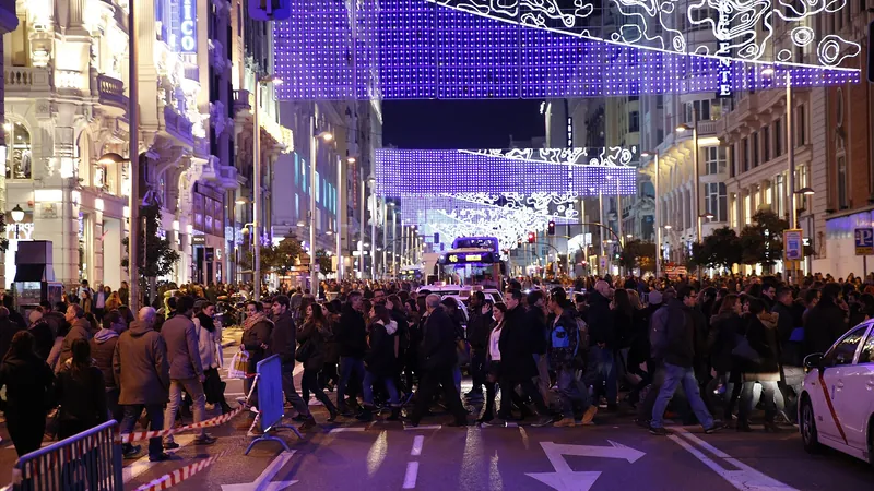 Calle comercial abarrotada bajo un techo de luces navideñas violetas por la noche