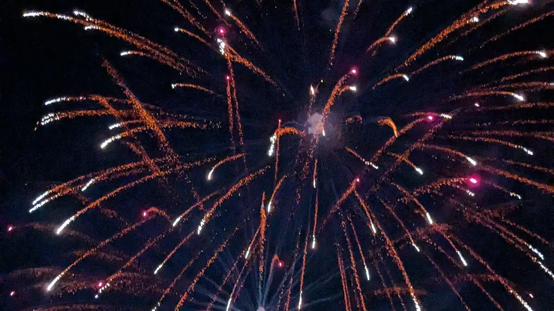 Fuegos artificiales blancos y azules estallando sobre las luces de una ciudad en Año Nuevo