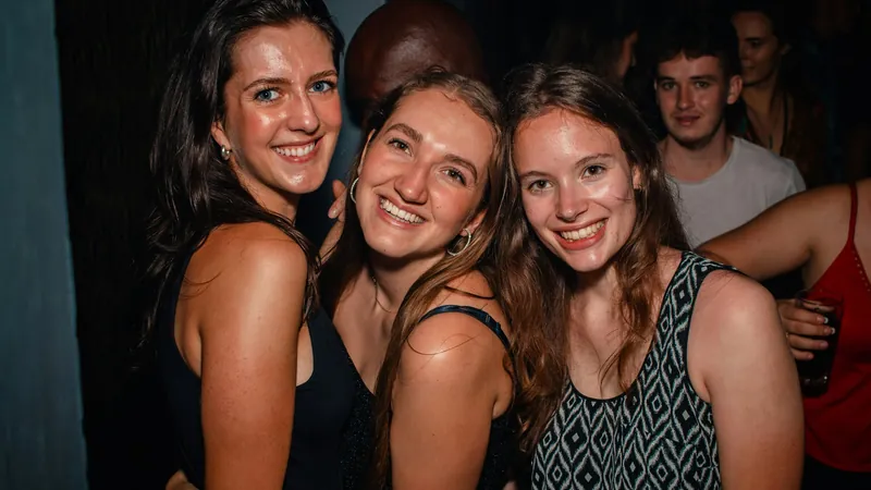 Tres amigas sonríen abrazadas durante una fiesta nocturna