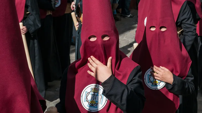 Nazarenos con capirote granate y escudo de la hermandad en una procesión de Semana Santa en Carmona