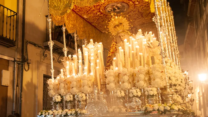 Paso de palio iluminado con velas recorriendo de noche una calle estrecha de Granada