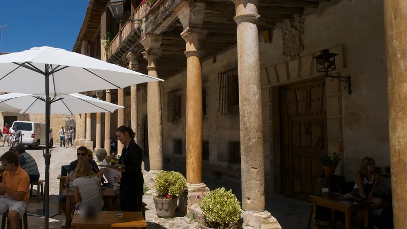 Terraza con sombrillas blancas bajo los soportales de piedra de la plaza mayor de un pueblo castellano